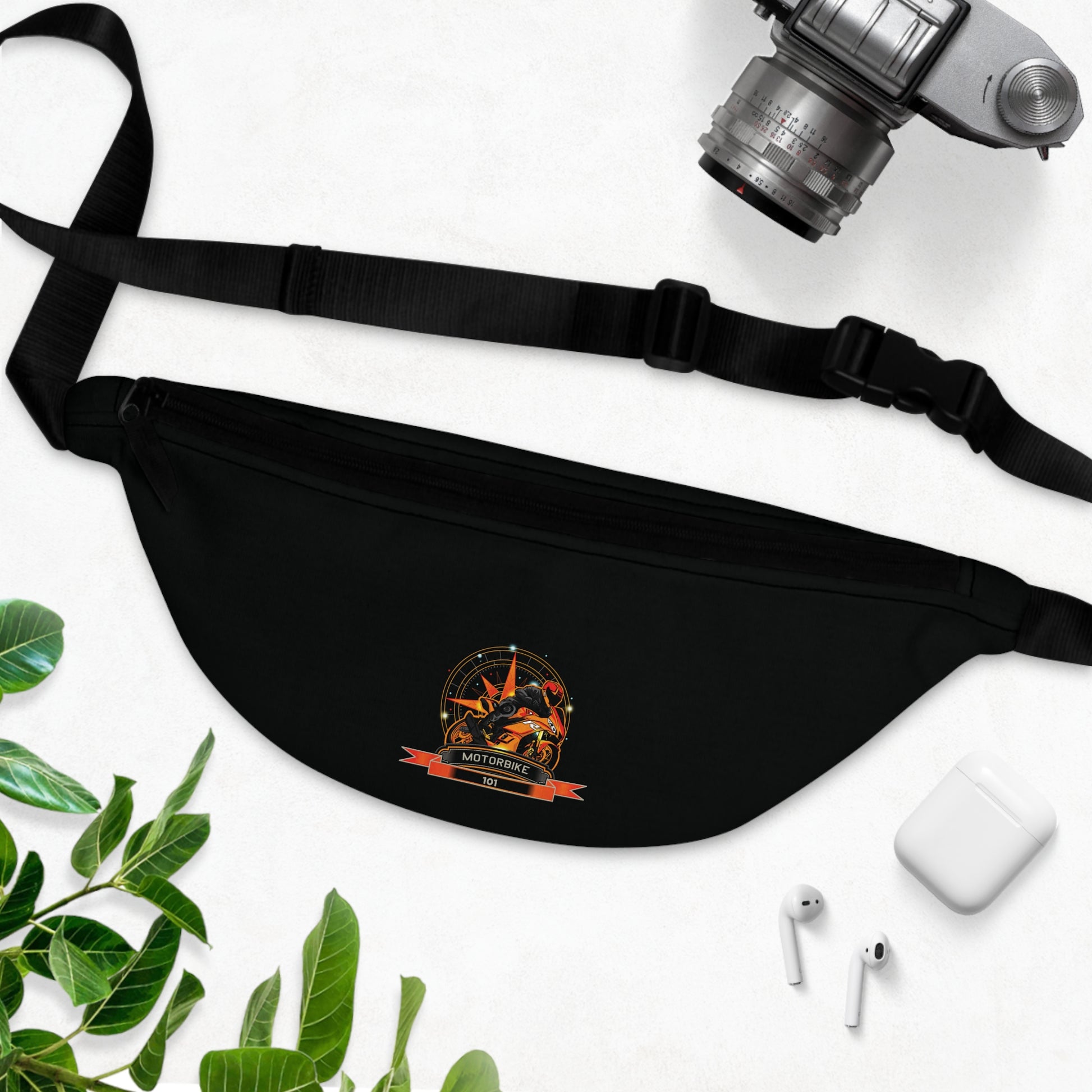 Black fanny pack with a logo on a white surface with a camera, phone, and leaves.